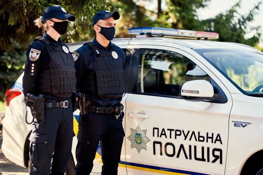 Двоє патрульних поліцейських у формі біля білого автомобіля патрульної поліції